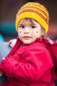 A young Aboriginal child dressed warmly while attending a public rally in Melbourne. Portrait of a young Aboriginal child wearing a yellow knitted beanie and red coat at a public rally in Melbourne, with face paint in the colours of the Aboriginal flag.