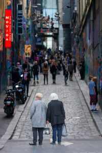 Two elderly women pause together at the entrance to Melbourne’s bustling Hosier Lane. Two elderly women standing together at the entrance to Hosier Lane in Melbourne, looking down the busy graffiti-covered laneway filled with people.