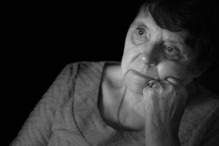 A reflective portrait of Eliza Whittaker gazing thoughtfully out a window while missing her husband, Graham. Black-and-white portrait of Eliza Whittaker resting her head on her hand while gazing thoughtfully toward a window in soft light.